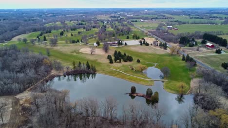 Sobrevuelo-Aéreo-De-Un-Campo-De-Golf-En-El-Campo-Con-Un-Lago-Durante-La-Primavera