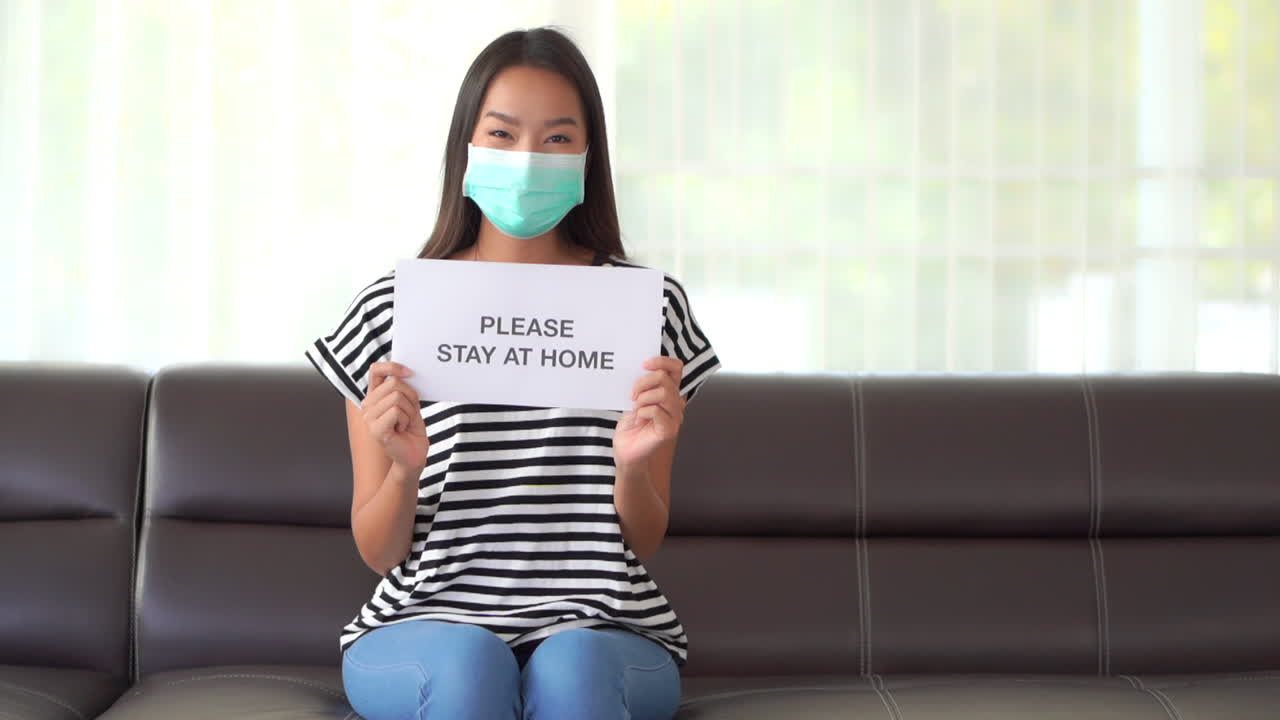 Asian Woman with Mouth Mask Holding Please Stay At Home Sign, Indoors
