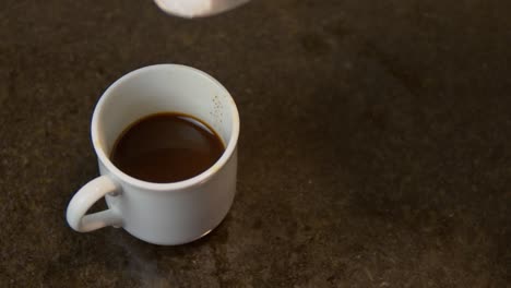 a cup of hot choco above the table dropped with white sugar by a man - close up shot