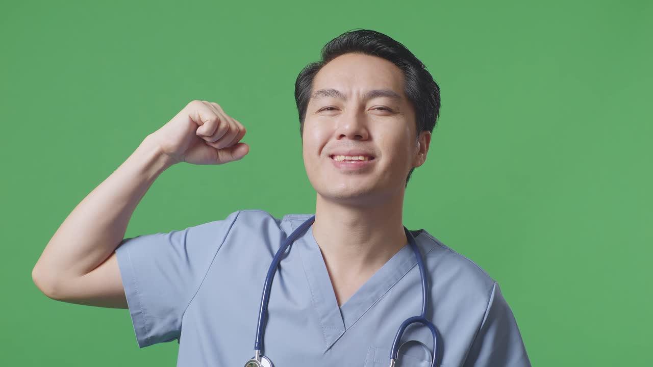 스테토스코프를 들고 있는 아시아 남성 의사의 근접 사진. 병원의 녹색 스크린 배경에서 미소와 근육을 구부리는 모습.