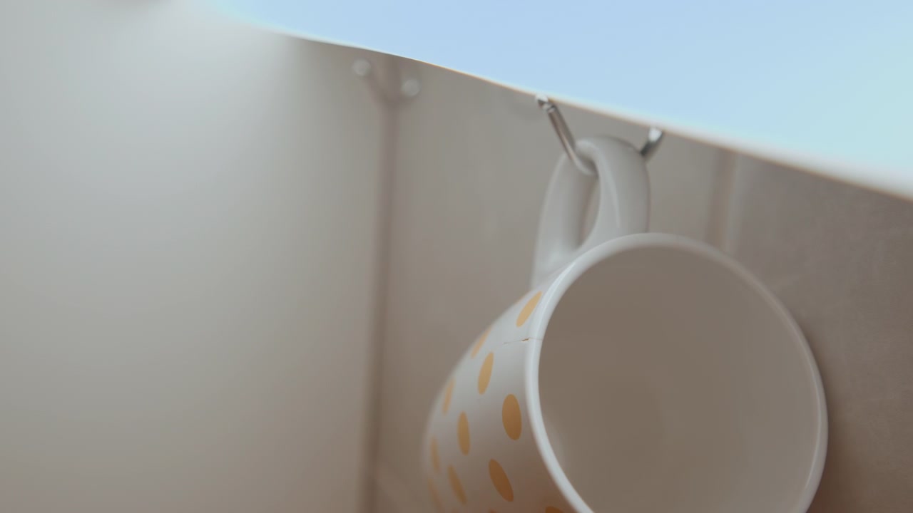 Calm morning routine involving drink preparation. Peaceful morning activity of setting up beverage essentials. Ensuring tranquil start by hanging mug and preparing morning refreshment calmly
