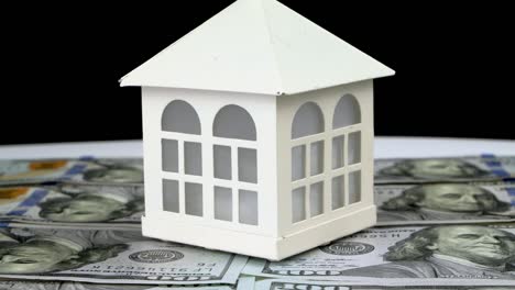 model of small familly house standing on background of dollars banknotes and rotate slowly.