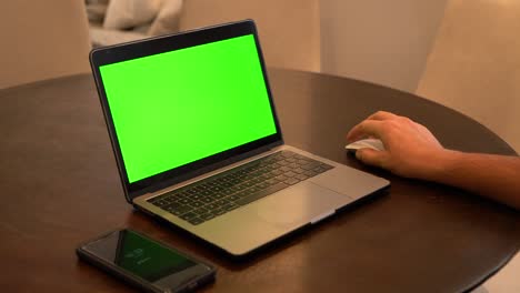 hombre usando laptop, celular en primer plano, pantalla verde