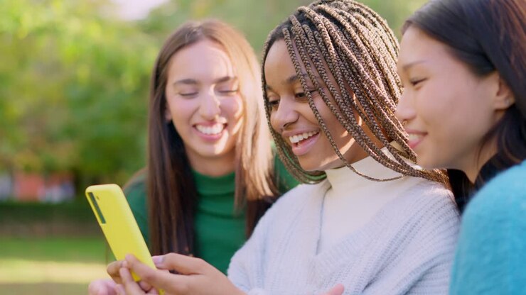 Multi-ethnic friends laughing and sharing content on a smartphone outdoors