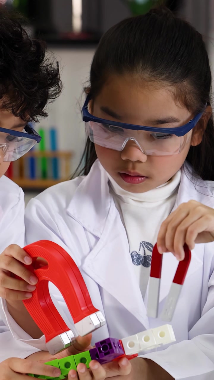 Siswa muda mengenakan jas lab menggunakan magnet untuk pembelajaran STEM di lingkungan kelas yang terang.