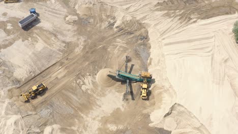 Top-aerial-view-of-bulldozer-loading-sand-into-empty-dump-truck-in-open-air-quarry