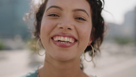 retrato en primer plano de una joven hispana linda que mira sonriendo alegremente a la cámara en el fondo de una ciudad soleada disfrutando del estilo de vida urbano