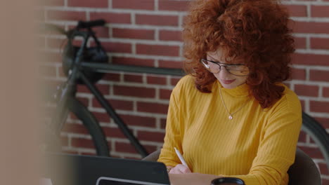 retrato elegante joven pelirroja mujer de negocios escribiendo notas haciendo lluvia de ideas creativas disfrutando de trabajar en una oficina moderna sonriendo feliz usando gafas