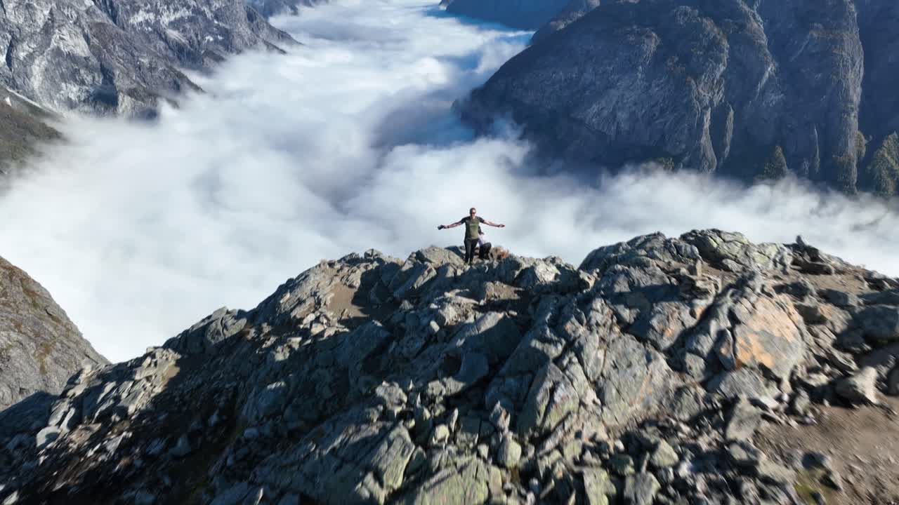Drone flies fast toward a couple at Bakkanosi cliff, tilting up to reveal the stunning fjord landscape as one person raises their arms in excitement