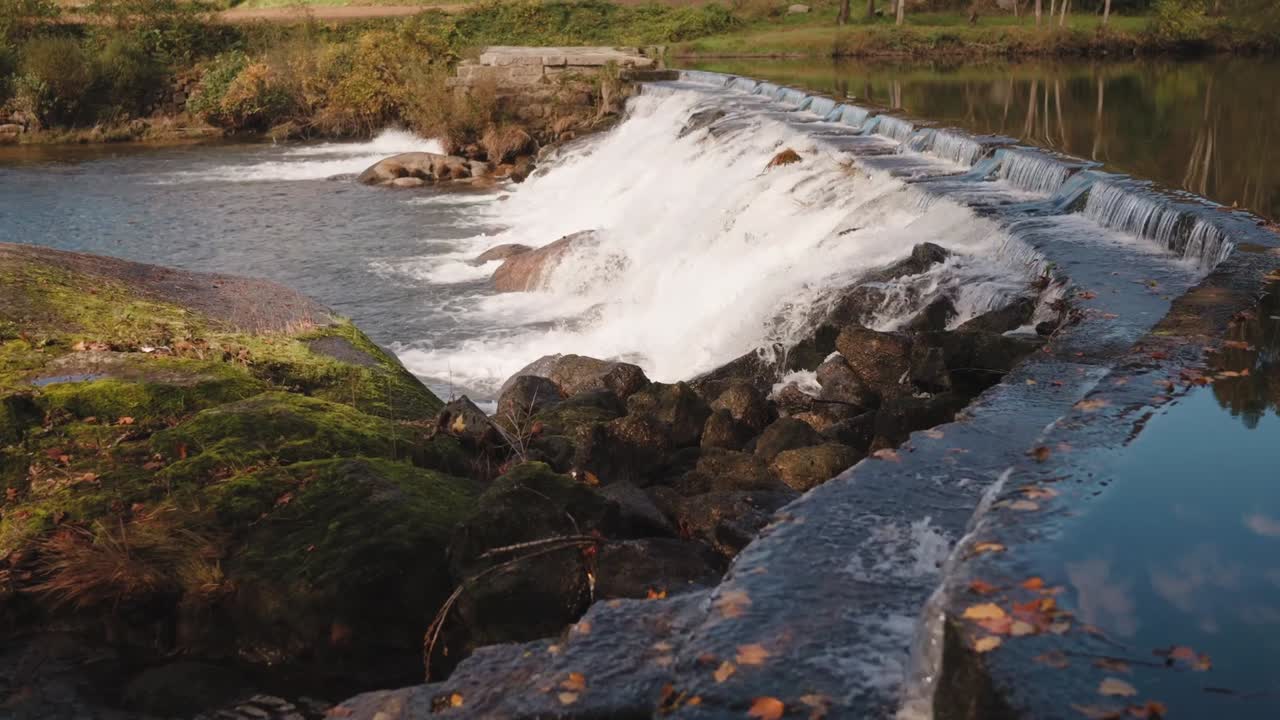 lite fossefall som kaskader over steiner med høstløv og rolig rennende vann i Minho, Nord-Portugal