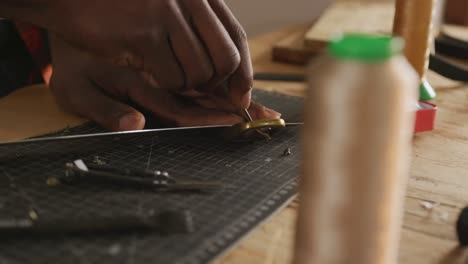 close up of hands of african american craftsman preparing belt in leather workshop