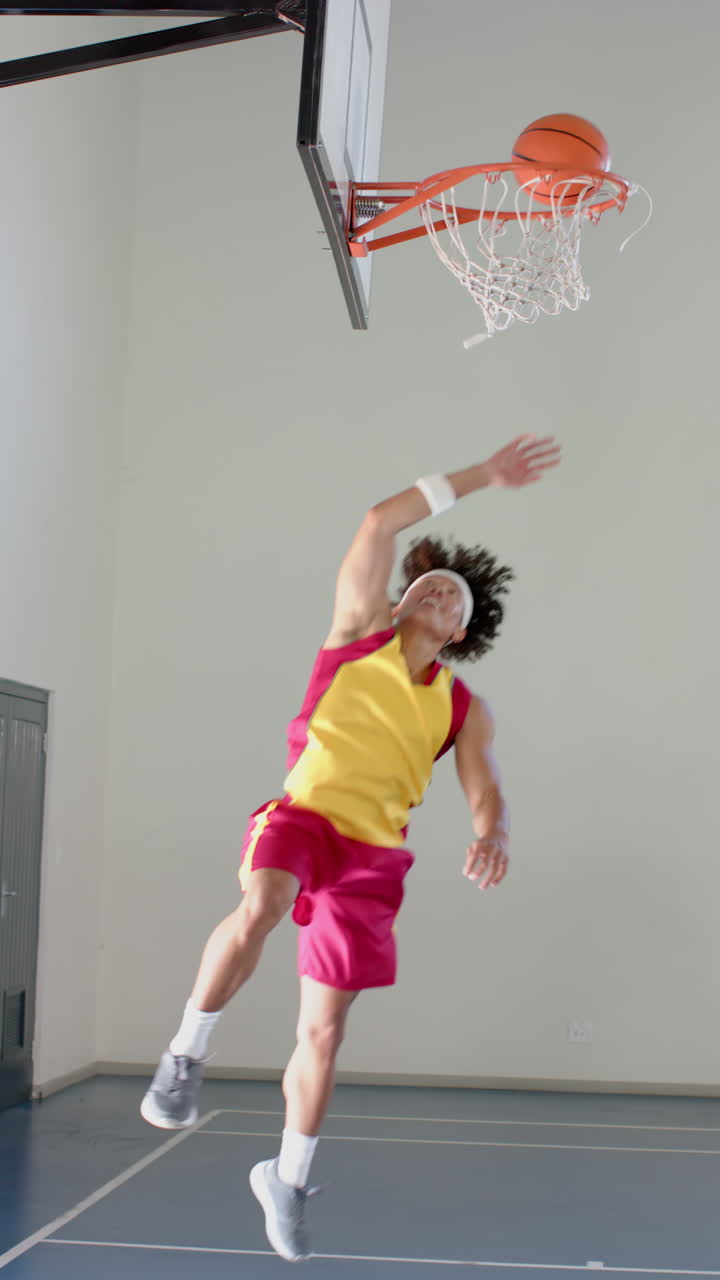 Vertical video: Playing basketball, man in sportswear jumping to score basket in gym