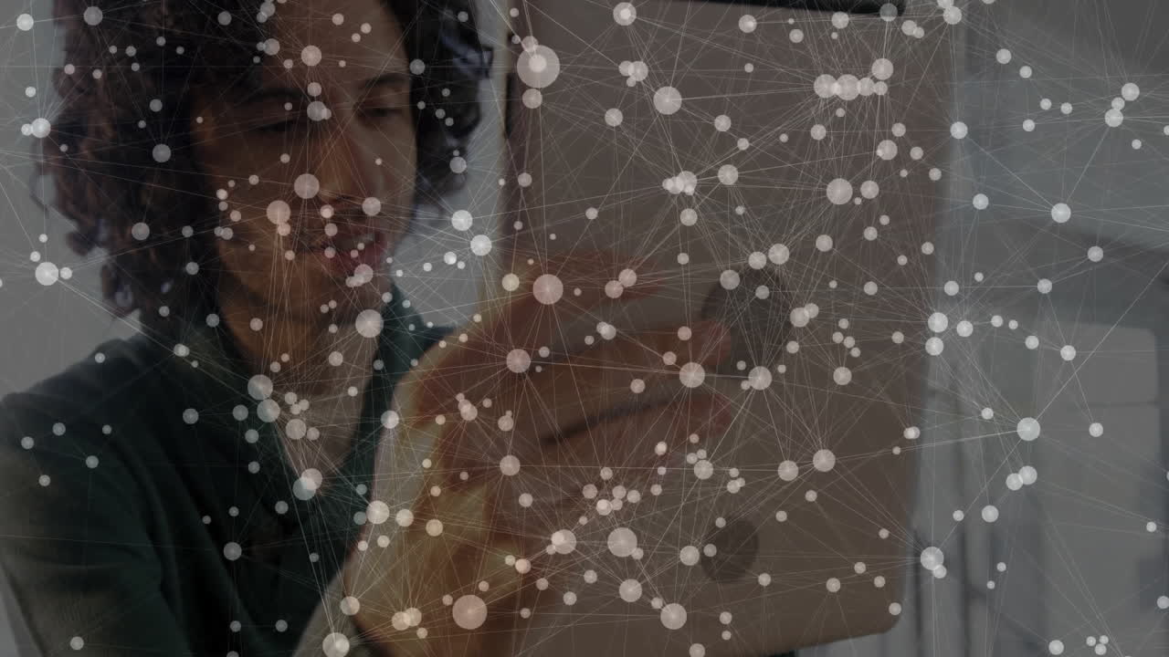 Male designer holding tablet inside tech office, showing animated network overlay connecting data