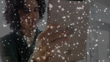 male designer holding tablet inside tech office, showing animated network overlay connecting data