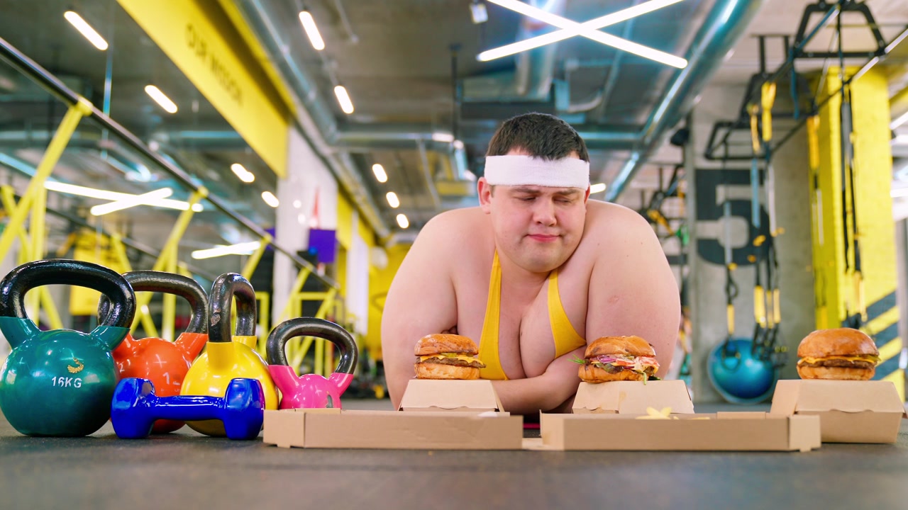 ジムでファストフードの誘惑と格闘する太りすぎの男性