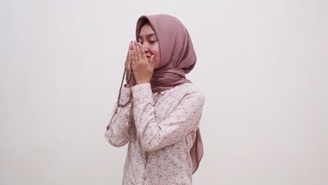 happy young asian muslim woman standing while praying using prayer beads