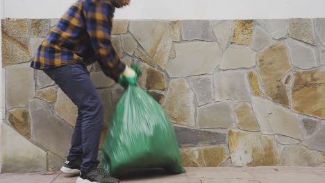 caucasian male picking up heavy garbage trash bag filled with biological food waste, recyclable bottles garbage