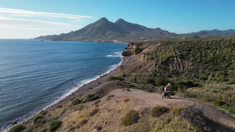 Woman-cuddles-dog-at-top-of-mountain-in-Cabo-de-Gata-National-Park,-Andalusia,-Spain---Aerial