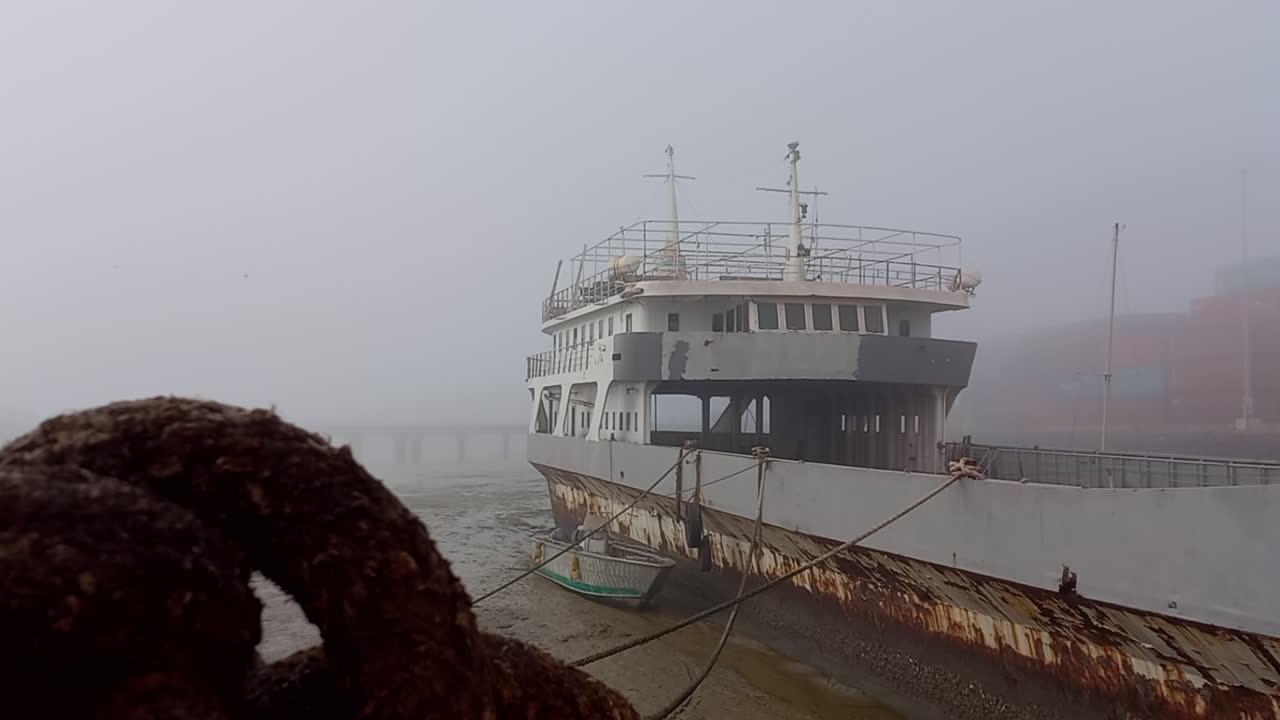 Old and large boat stranded in the fishing port of Bissau, close-up of the rope knot with the boat and morning fog