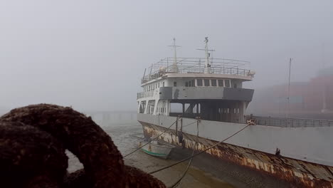 old and large boat stranded in the fishing port of bissau, close-up of the rope knot with the boat and morning fog