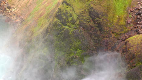 Mist-from-Yellowstone's-Upper-Falls-blows-against-moss-covered-cliff-face