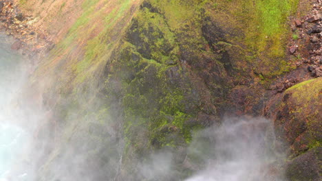 mist from yellowstone's upper falls blows against moss-covered cliff face