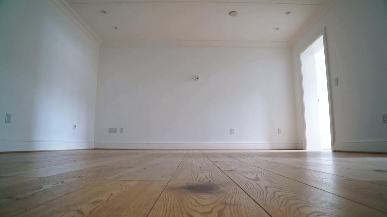Operator lifting low camera from floor in empty room, revealing wood grain and bright doorway