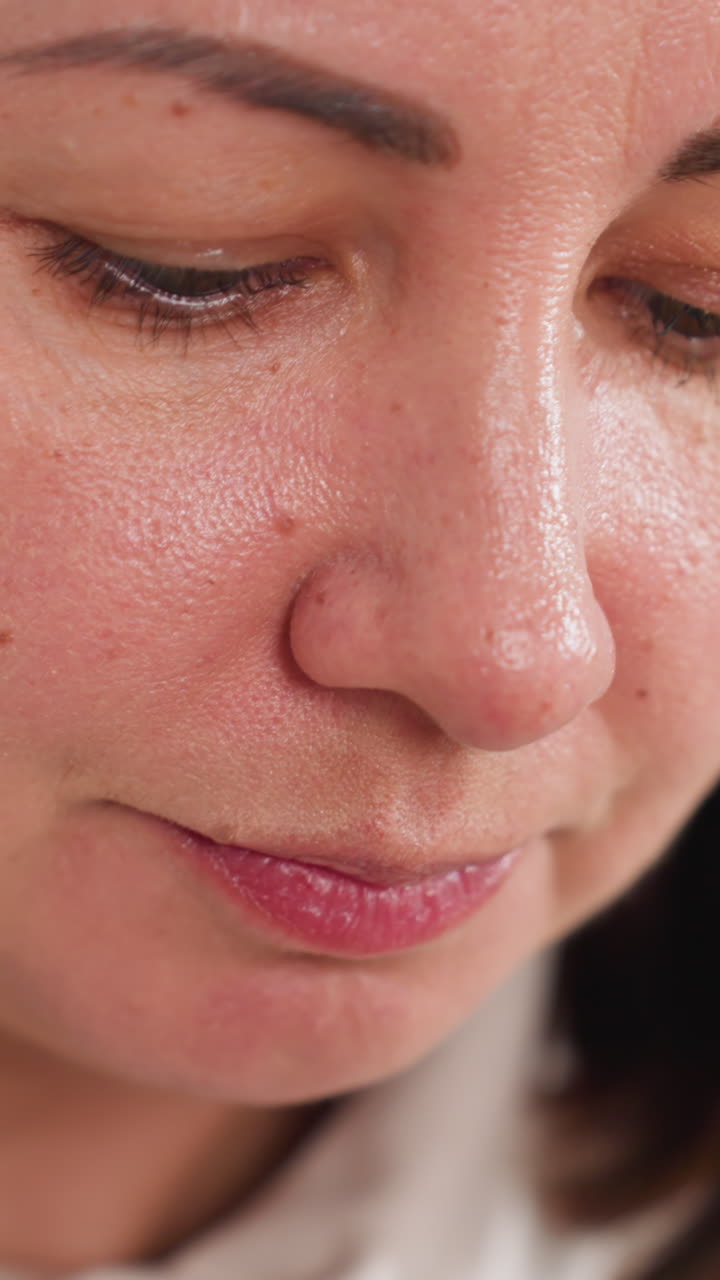 primer plano íntimo del rostro de una mujer blanca con piel brillante, expresión pensativa durante un momento de degustación tranquilo, un dedo acercando una pequeña nuez a los labios, masticación lenta, mirada enfocada hacia abajo, ambiente interior natural