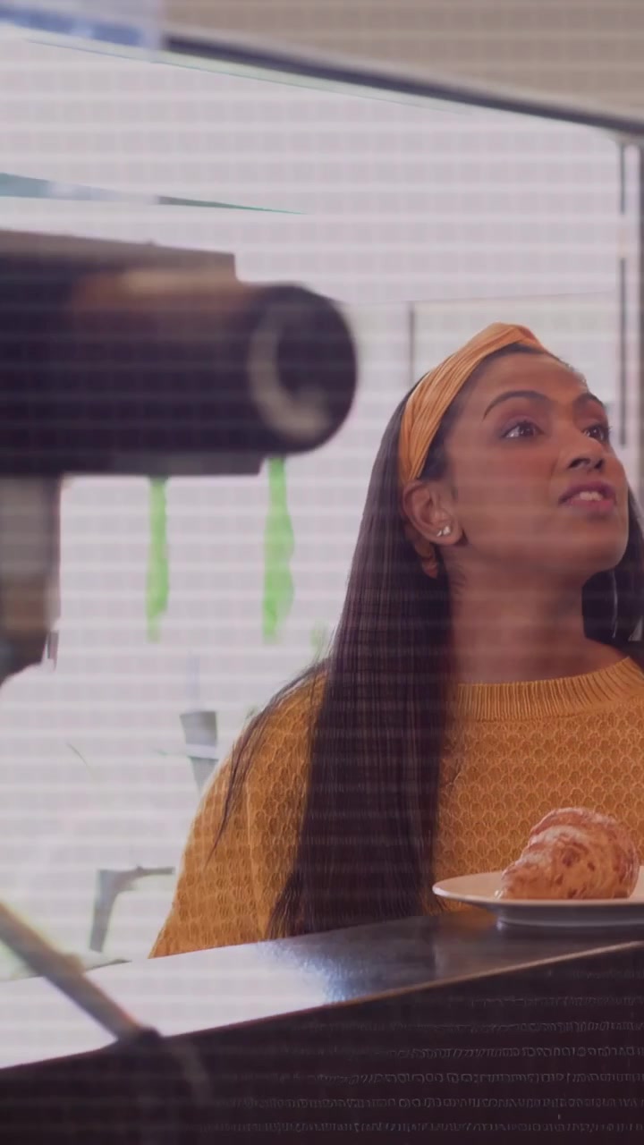 Video verticale: Donna seduta al caffè che ascolta grafici tecnologici vocali su uno schermo di vetro, prendendo il telefono e controllandolo.