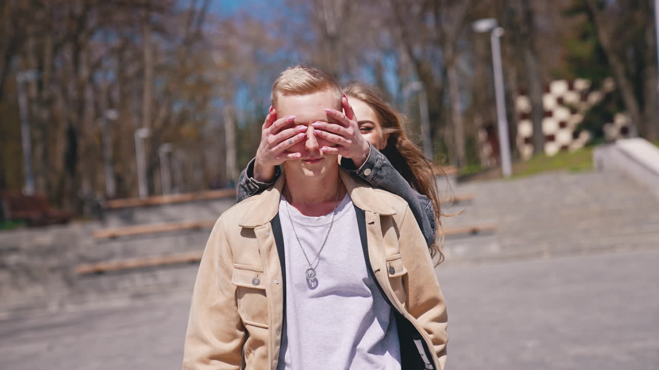 Guess who. Happy couple in love meeting in the park. Woman closed eyes of her boyfriend while standing behind him. Romantic date concept