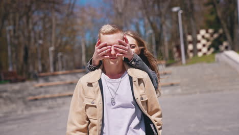 guess who. happy couple in love meeting in the park. woman closed eyes of her boyfriend while standing behind him. romantic date concept