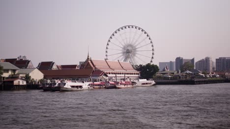 riverfront scene with ferry boats, temple, and ferris wheel
