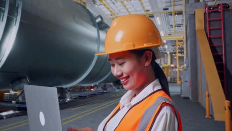 close up side view of asian female engineer with safety helmet working on a laptop while standing in pipe manufacturing factory
