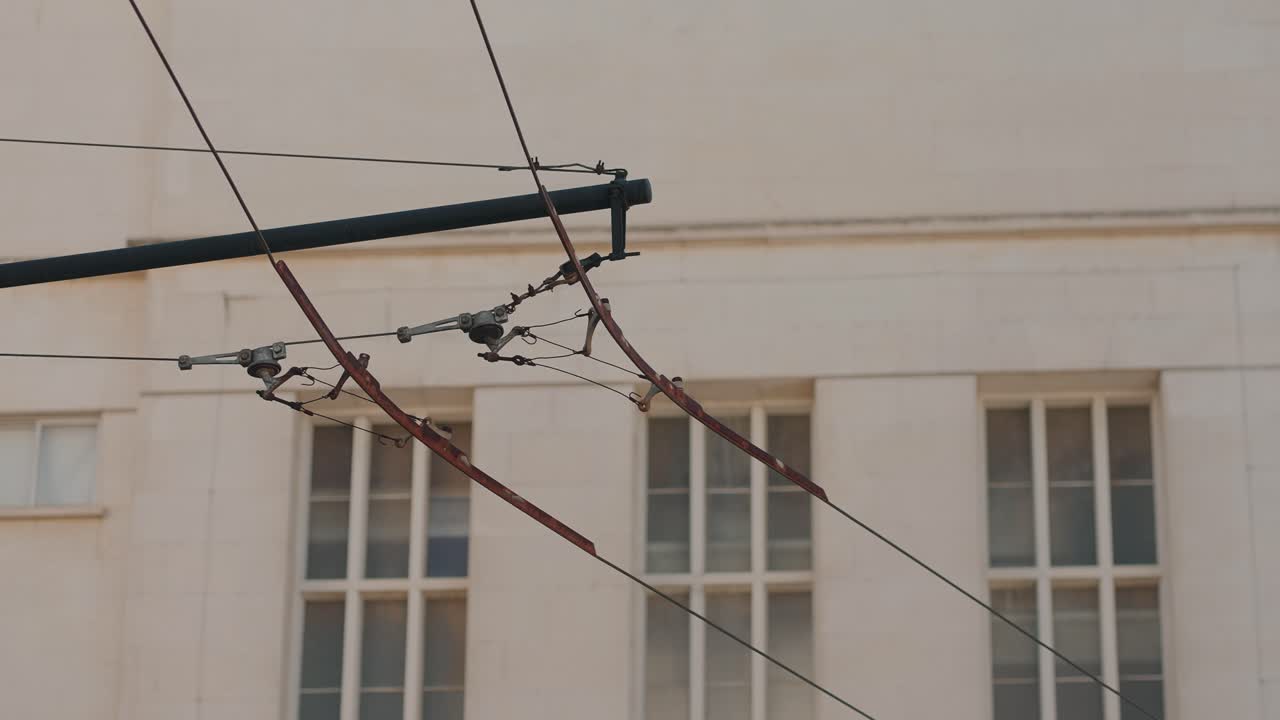 Overhead trolley wire cables against Coimbra University building with window backdrop