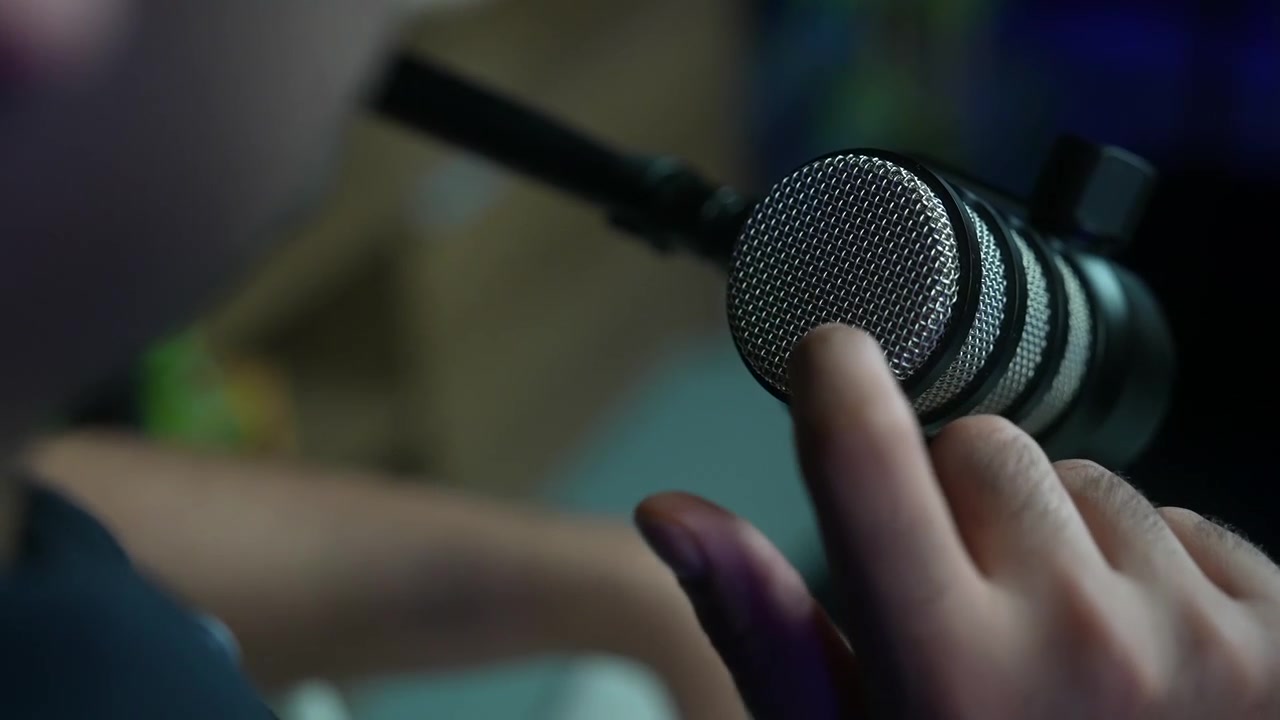 slow motion of presenter finger touching the metallic mesh grille of a professional microphone in a podcast studio. Sound testing, audio engineering and broadcast setup concept.