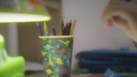 child drawing at night on his desk and coloring with colored paints