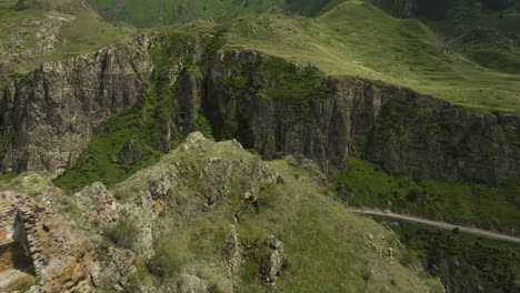 Volando-Sobre-La-Fortaleza-En-Ruinas-De-Tmogvi-En-La-Cima-De-La-Montaña-Con-Una-Carretera-Escénica-En-El-Fondo