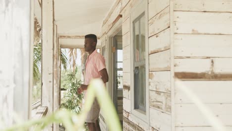 Afroamerikanischer-Mann,-Der-Sich-In-Der-Morgensonne-Auf-Der-Veranda-Eines-Hölzernen-Strandhauses-Ausdehnt,-Zeitlupe