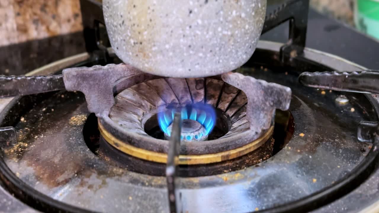Macro shot of blue gas flame heating a metal pot on a stovetop. Perfect for cooking, wellness, herbal tea, and home remedy process visuals