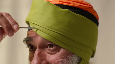 fotografía de estudio de cerca de un anciano sikh con barba usando la aguja salai al ponerse el turbante contra un fondo plano