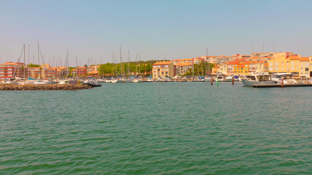 Zoom in shot of waterfront residential buildings and moored boats at Cap d'Agde marina on a summer day