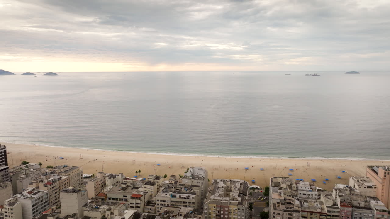 Copacabana beach in Rio de Janeiro, dense cityscape meets famous sandy shore, Atlantic Ocean under cloudy sky, Brazil. Aerial forward, copy space