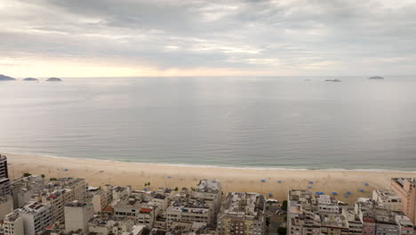 copacabana beach in rio de janeiro, dense cityscape meets famous sandy shore, atlantic ocean under cloudy sky, brazil. aerial forward, copy space