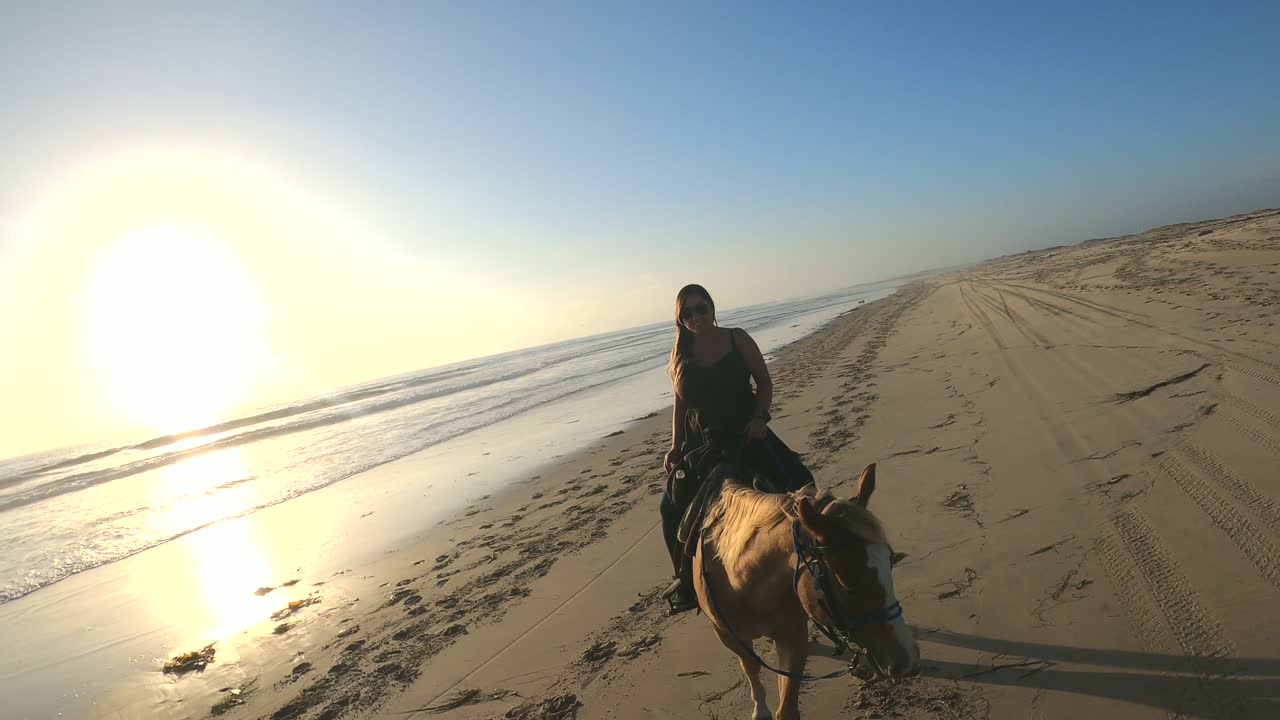 mulher bonita andando a cavalo na praia durante o pôr do sol