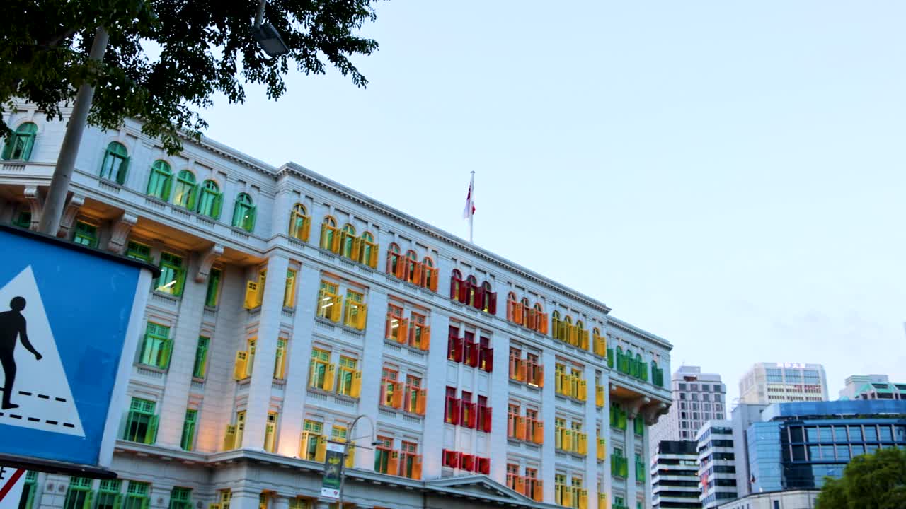 A daylight pan reveals a vibrant colonial building with multicolored windows and pedestrian signs in an urban Singapore setting, under clear skies
