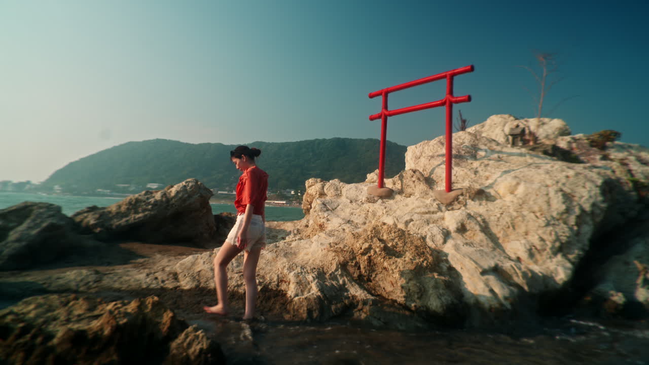 Woman walking towards a torii gate on a rocky beach