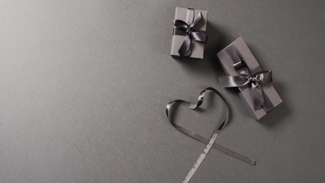 overhead view of two black gift boxes and ribbon in heart shape, on dark grey with copy space