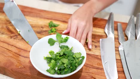 a person chops fresh coriander on a wooden board with precision, using a sharp knife in a well-lit kitchen