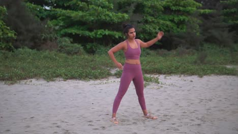 vista frontal de una mujer de meditación de yoga haciendo estiramientos y extensiones con vista al bosque detrás de ella sobre la arena