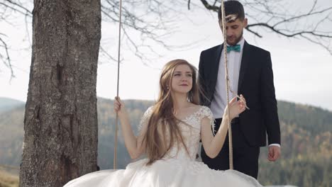 newlyweds. caucasian groom with bride ride a rope swing on a mountain slope